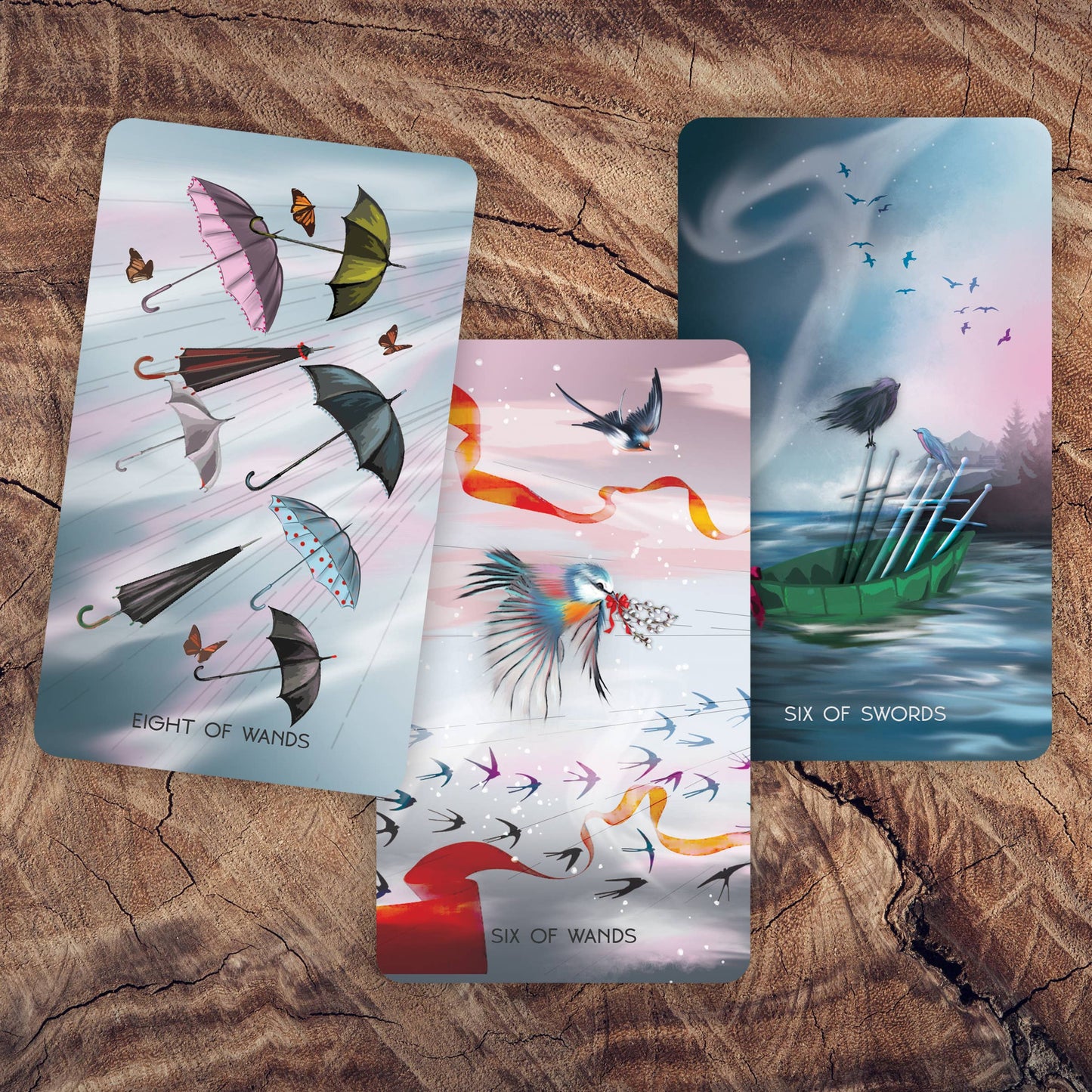 Three tarot cards with artistic designs on a wooden surface