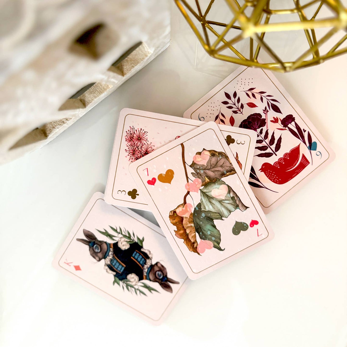 Set of playing cards with floral and nature-themed designs on a light surface.