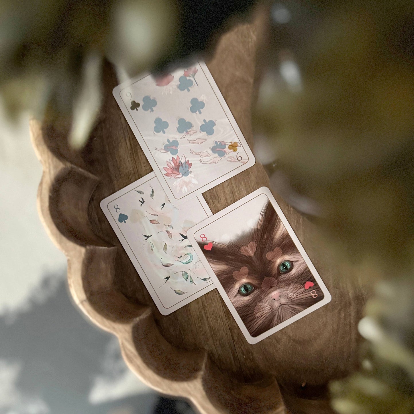 Three playing cards with floral designs and a cat's face on a wooden surface.