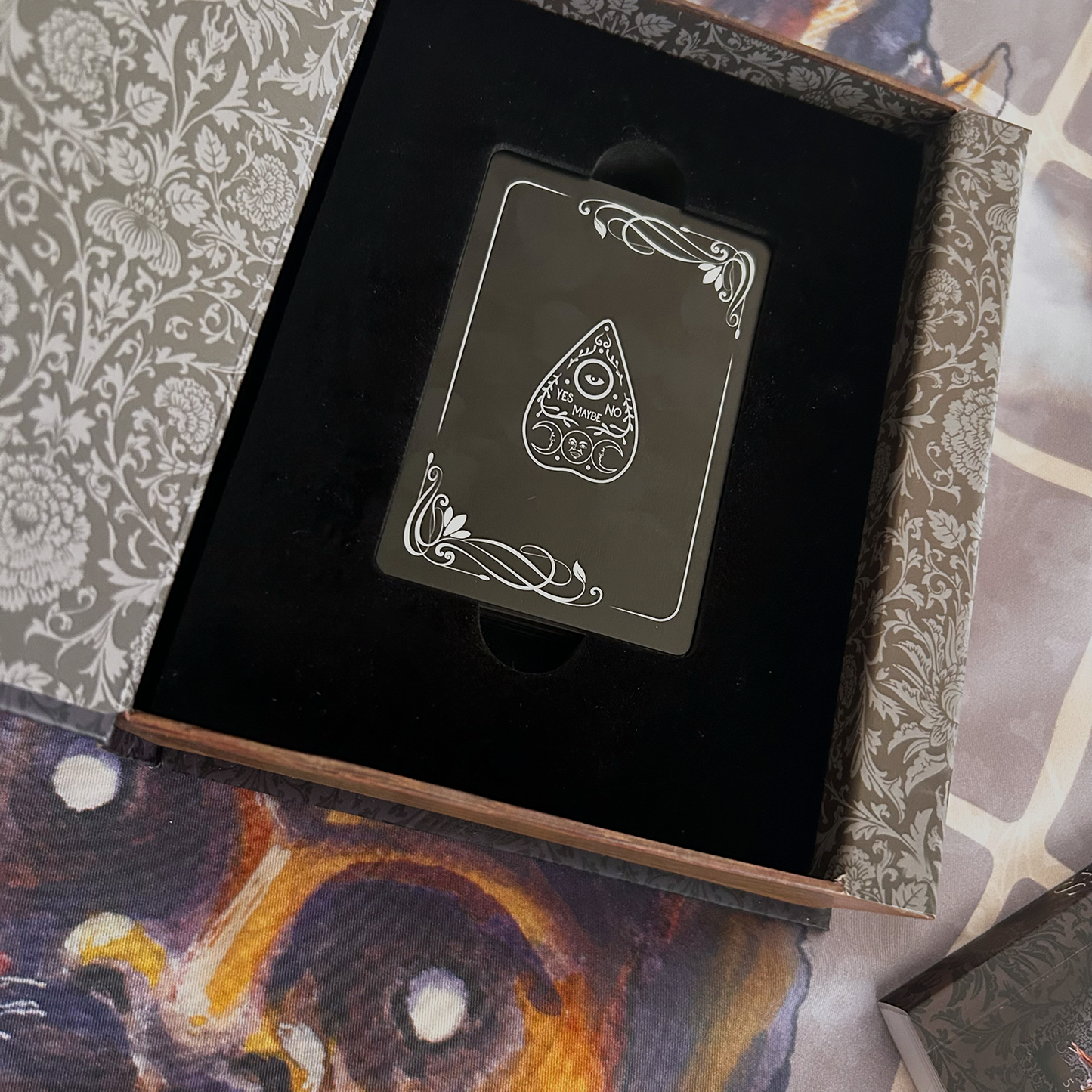 Black playing card with white design in an open ornate box.