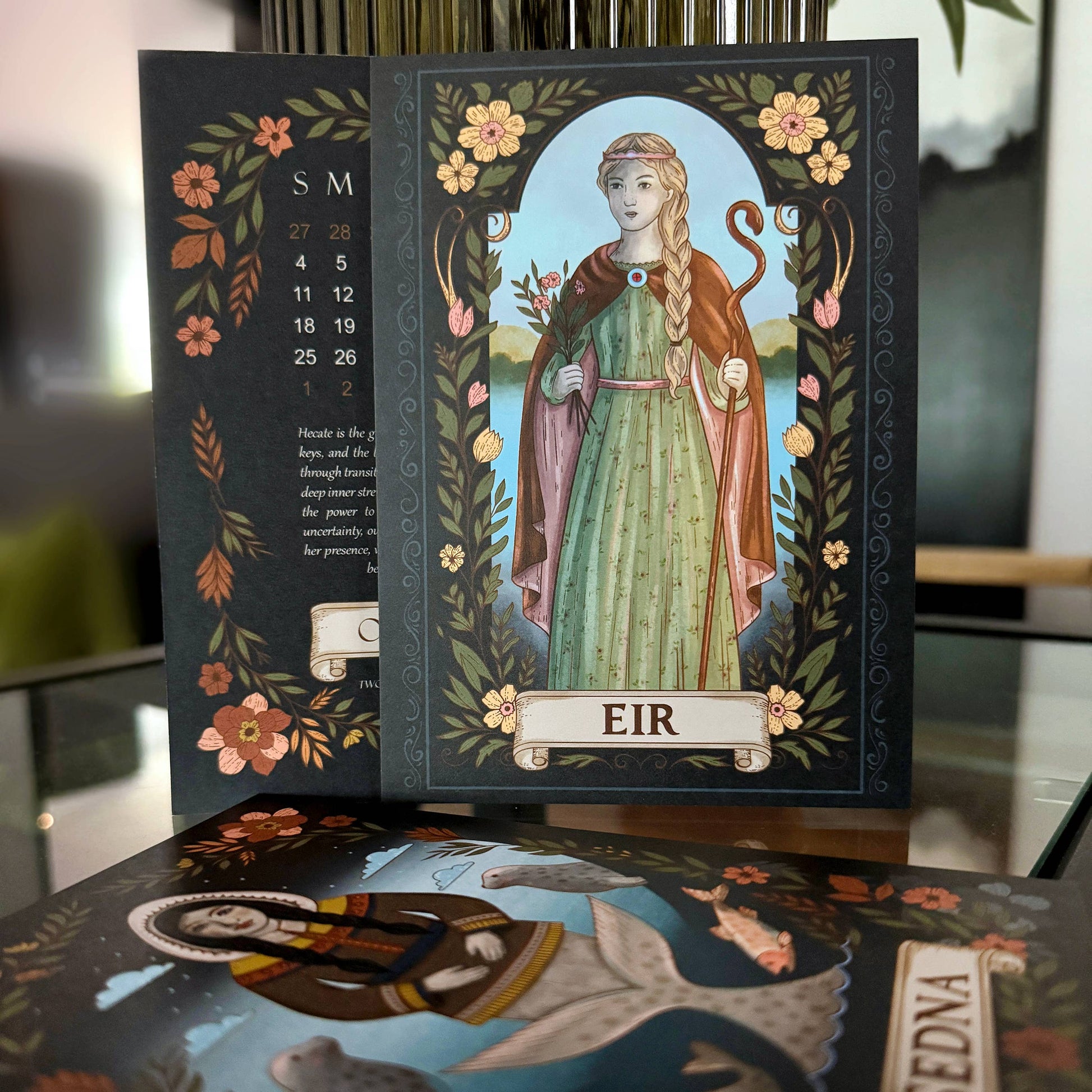 Decorative calendar with illustrations of people and flowers on a reflective surface.