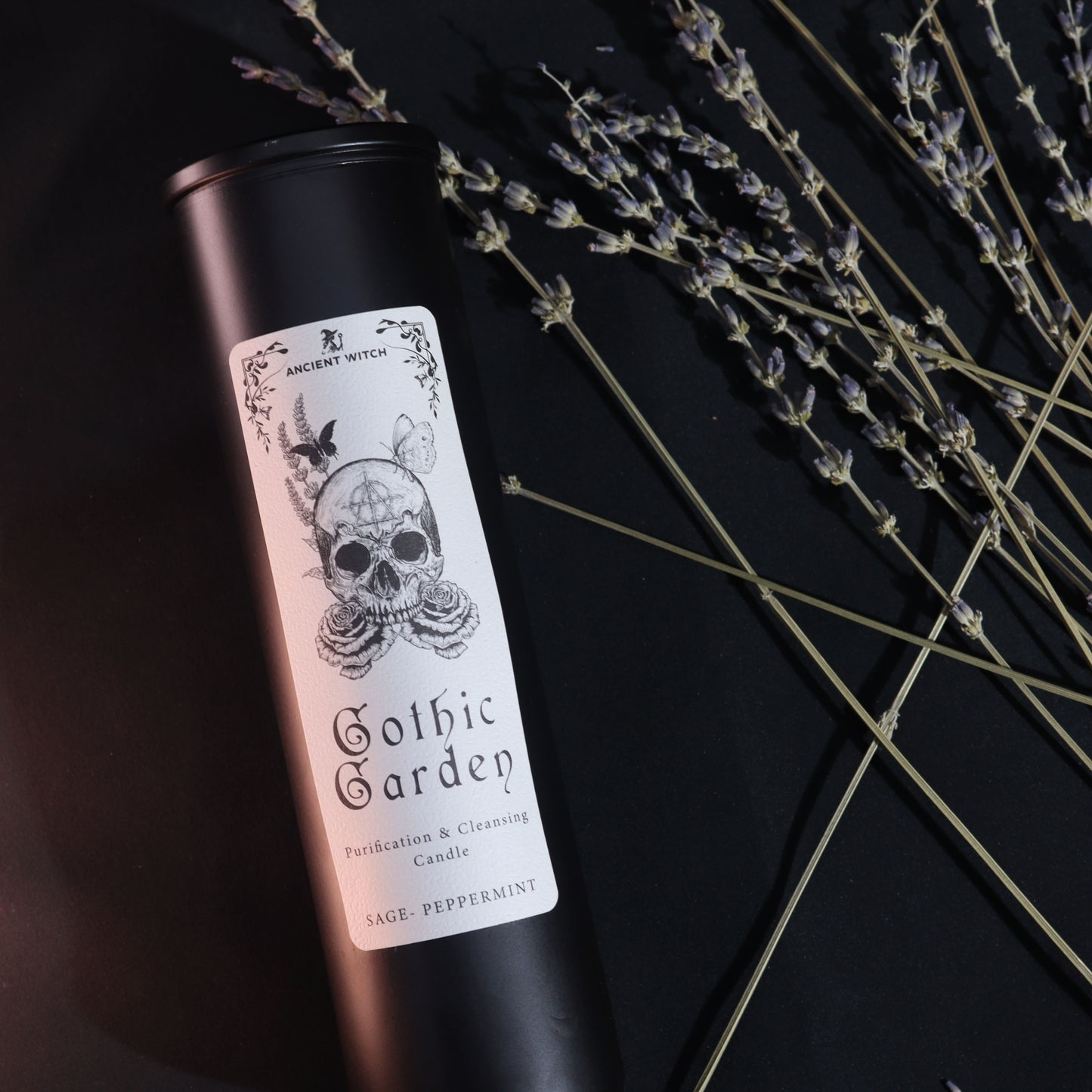 Candle in a black tin with a skull design on the label, set against a dark background with lavender.
