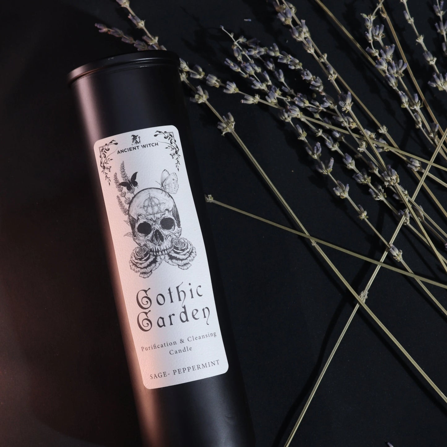 Candle in a black tin with a skull design on the label, set against a dark background with lavender.