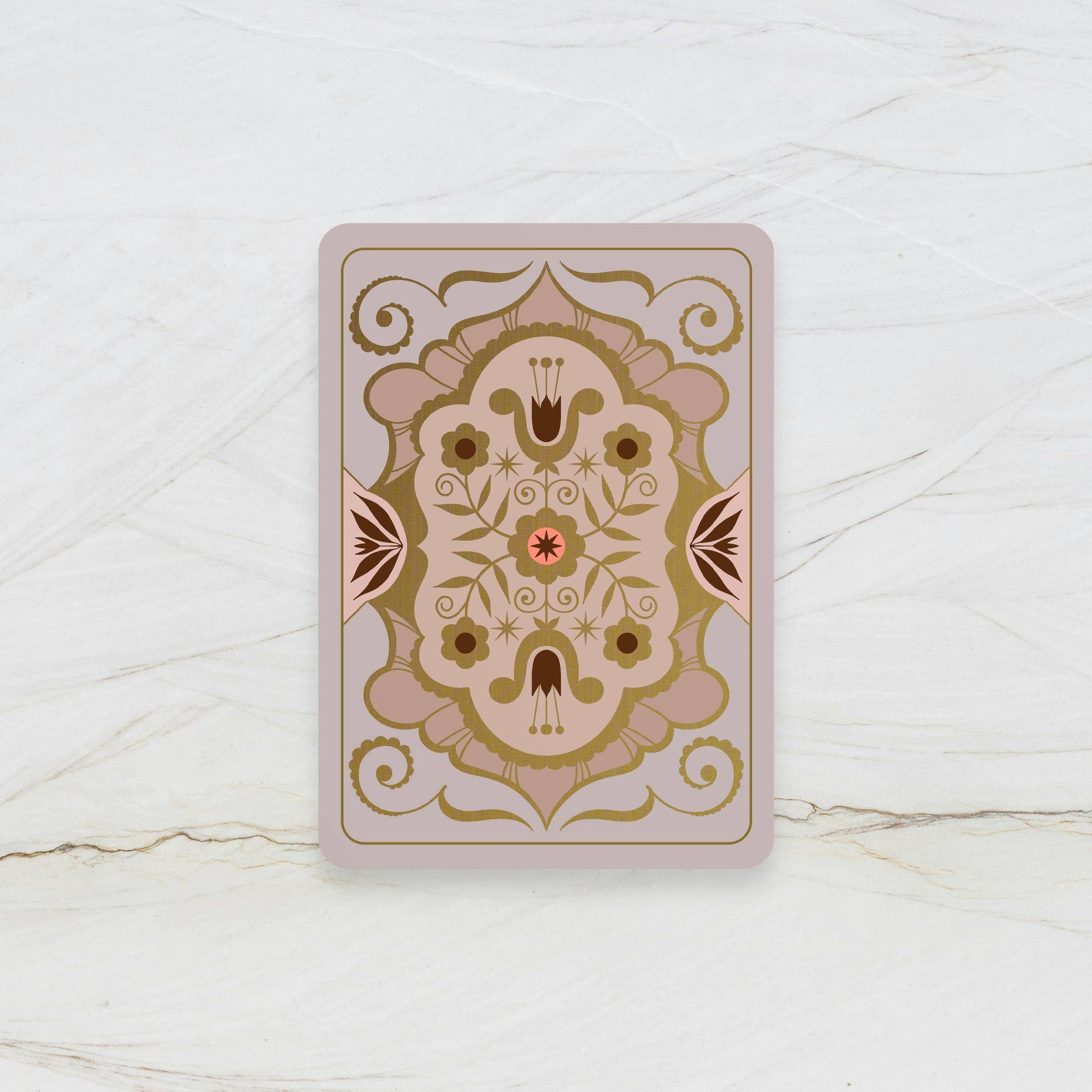Decorative playing card with intricate gold and brown design on a white marble surface