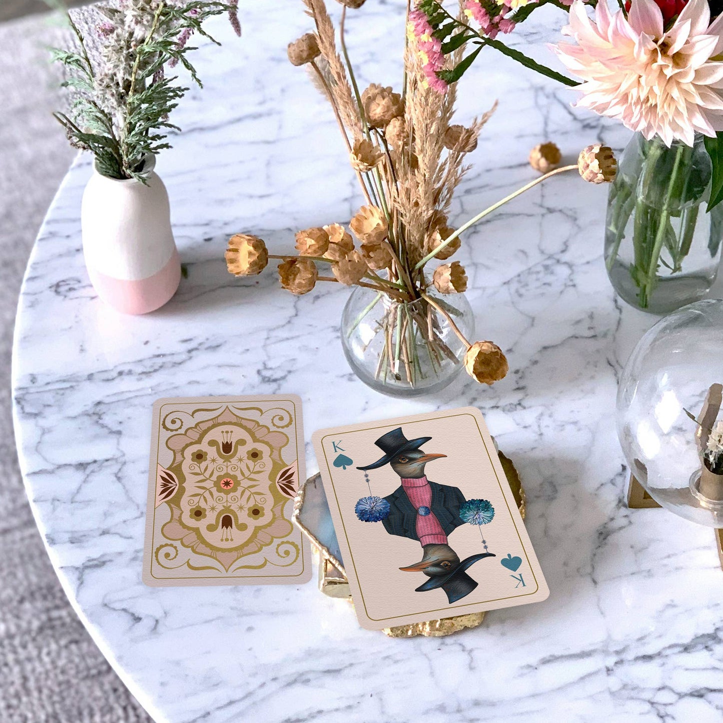 Two playing cards on a marble table with decorative vases and flowers.