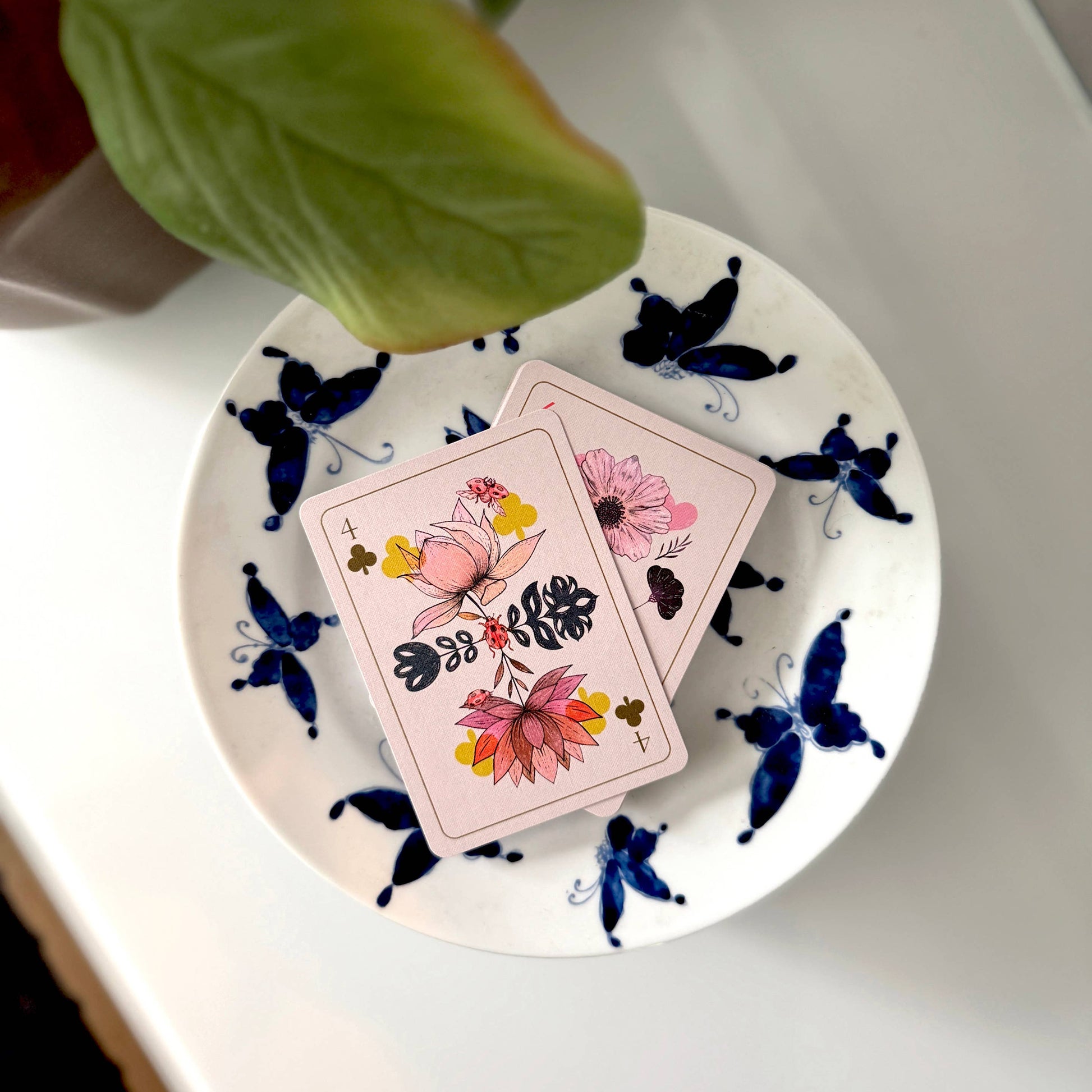 Two playing cards with floral designs on a white plate with butterfly patterns, held by a hand.