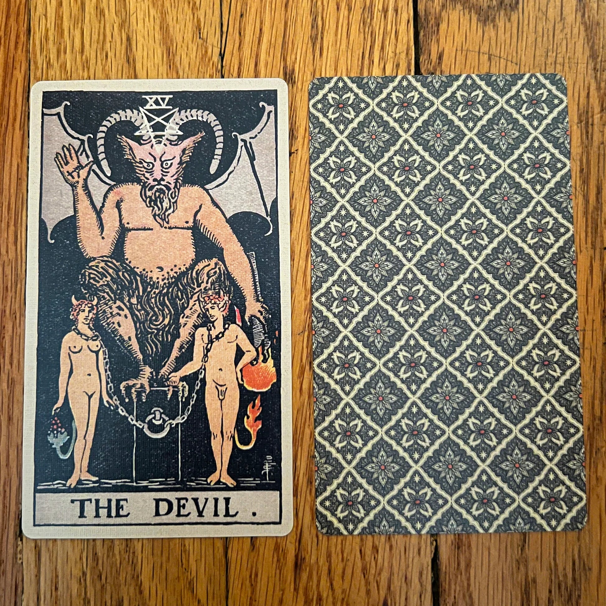 Tarot card featuring 'The Devil' with a patterned back on a wooden surface