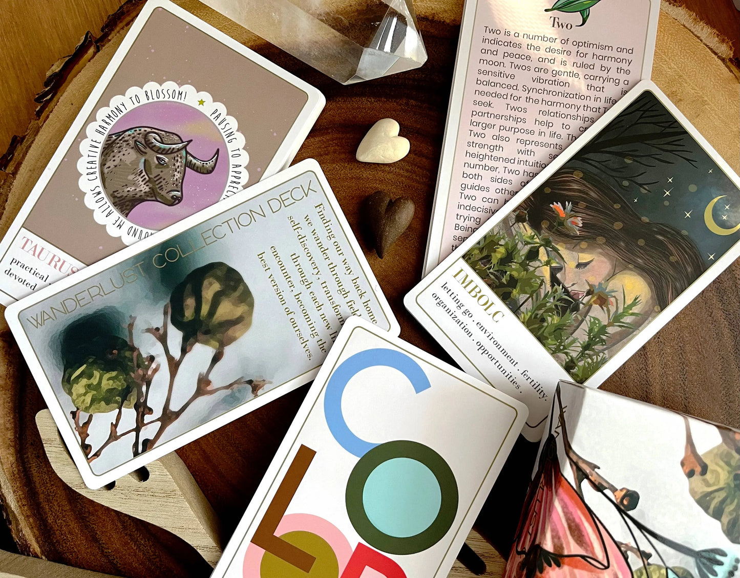 Collection of tarot cards on a wooden surface with a book open to a page. Wanderlust collection oracle deck