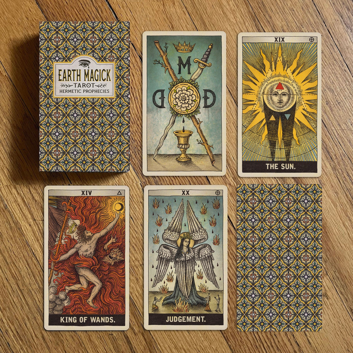 Earth Magick Tarot deck displayed on a wooden surface, showing the patterned box, several illustrated tarot cards, and one card face down. Visible card titles include The Sun, King of Wands, and Judgement.