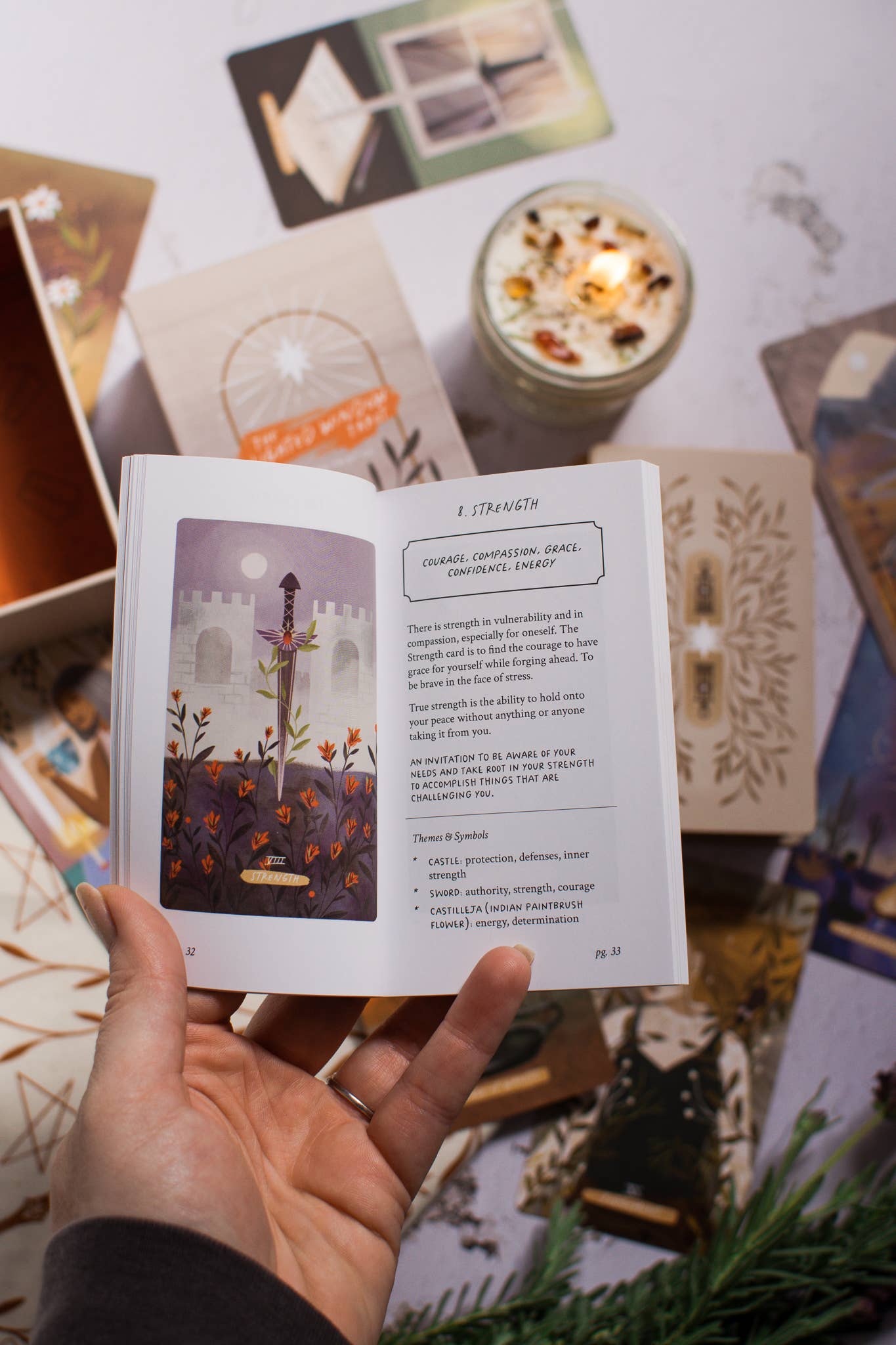 Hand holding an open book with a candle and tarot cards in the background