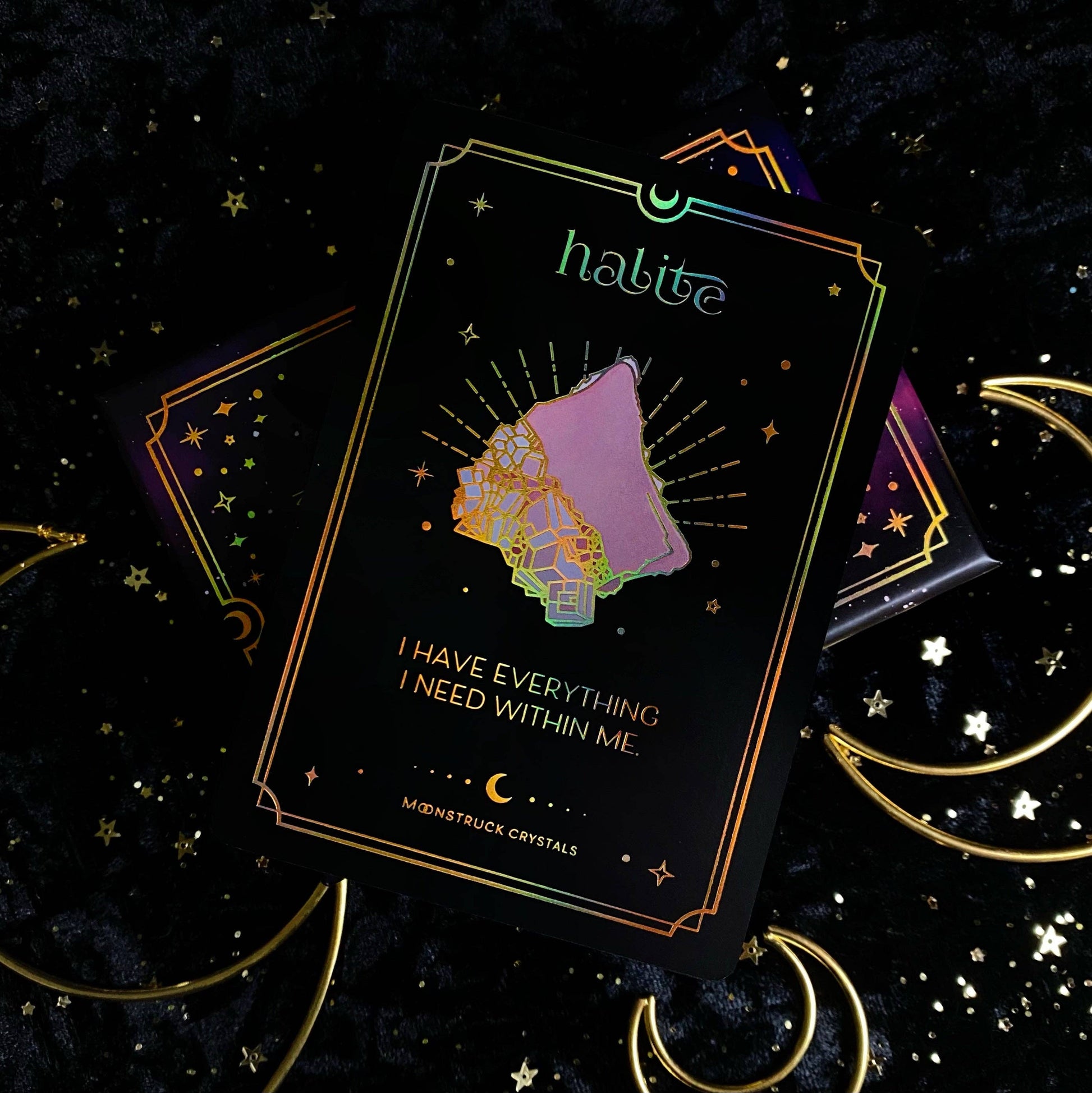Decorative card with 'halite' branding and celestial design on a dark background with stars and moon symbols. Gold Crystal Affirmations Golden Aura Edition featuring luxury affirmation cards inspired by crystal wisdom, mindfulness, and positive daily intentions.