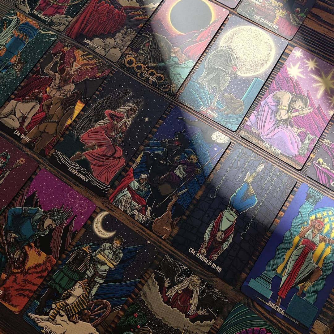 Collection of tarot cards with colorful illustrations on a wooden surface Dark reflections tarot by La Muci Available at Oneness Emporium