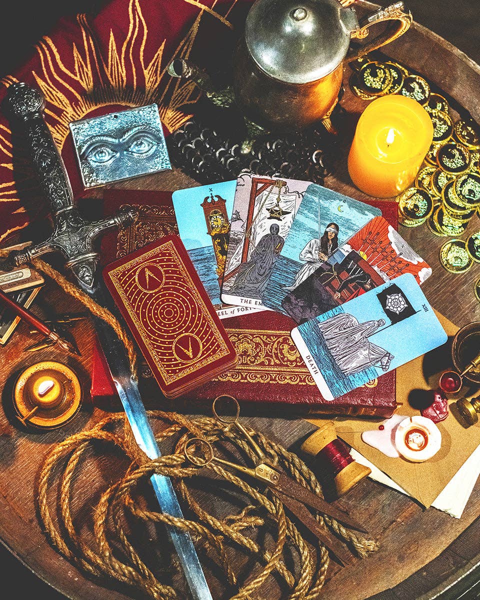 Spells and rituals items including tarot cards, candles, and a sword on a wooden surface.