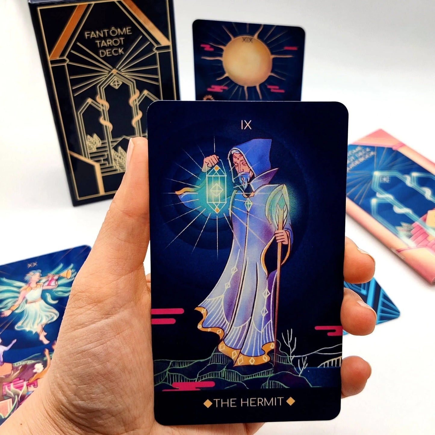 Hand holding a tarot card titled 'The Hermit' from the Fantôme Tarot Deck with other cards in the background.