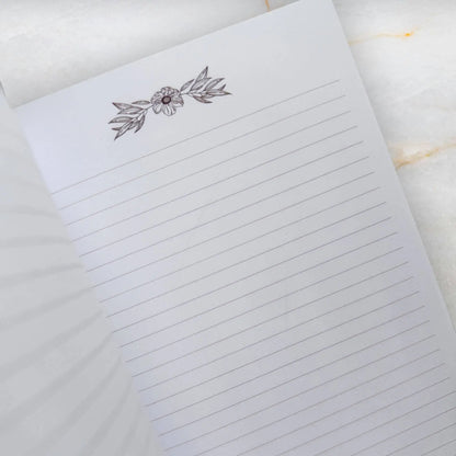 Notebook with floral design on the cover on a marble surface Meraki workbook for tarot and crystal work 