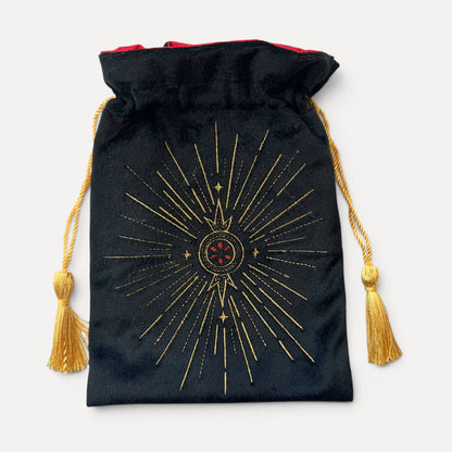 A black velvet drawstring pouch with a gold sunburst design and a red gem motif in the center, featuring gold tassel ties and a red lining.