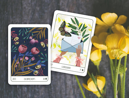 Two tarot cards with floral and butterfly designs on a dark surface with yellow flowers.