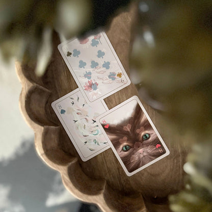 Three playing cards with floral designs and a cat's face on a wooden surface.