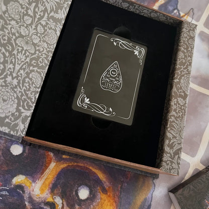 Black playing card with white design in an open ornate box.