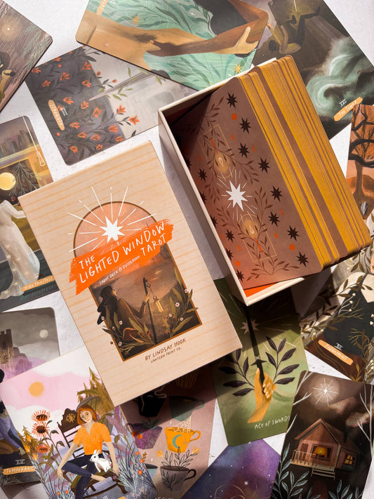 Collection of tarot cards and a box labeled 'The Lighted Window Tarot' on a colorful background.