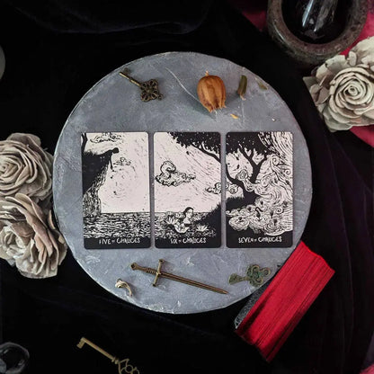 Triptych tarot card set on a round stone surface with decorative items.
