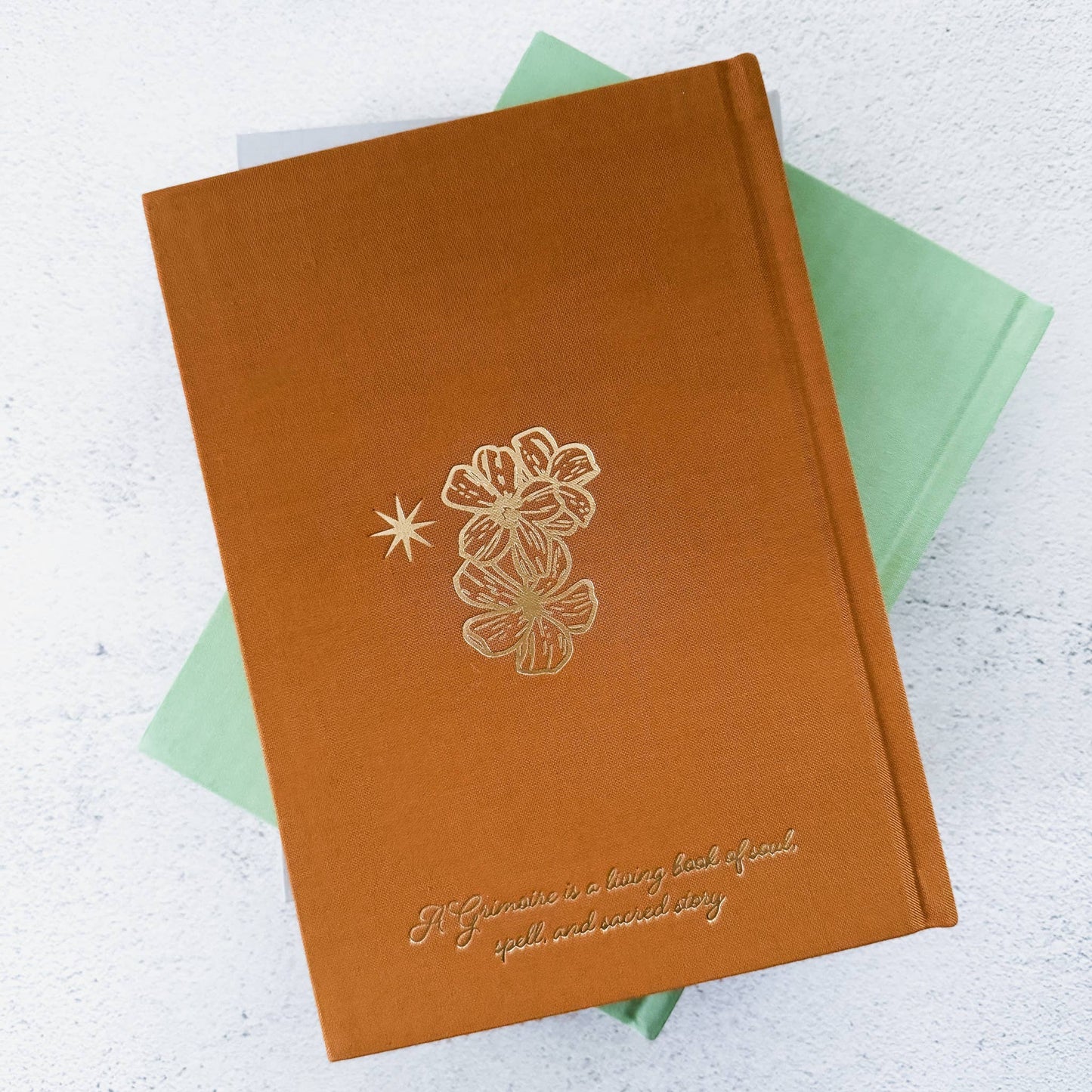 Brown notebook with floral design and text on a light gray background Grimoire Bouchette and Co Oneness Emporium