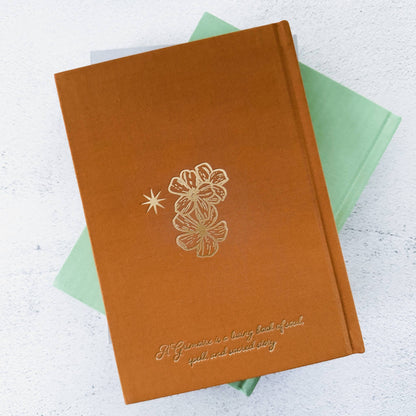 Brown notebook with floral design and text on a light gray background Grimoire Bouchette and Co Oneness Emporium
