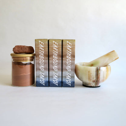 Three books titled 'Earthbound Tarot' with a jar and a stone on a white background