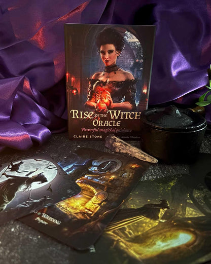 The book 'Rise of the Witch Oracle' by Claire Stone is displayed upright, surrounded by its illustrated oracle cards, a black cauldron, and draped purple silk fabric.