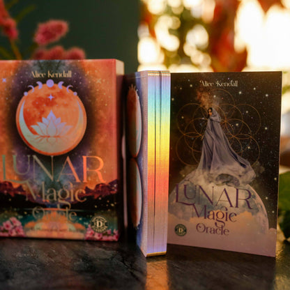 Two books titled 'Lunar Magic Oracle' by Alice Kendall on a reflective surface with a blurred floral background.