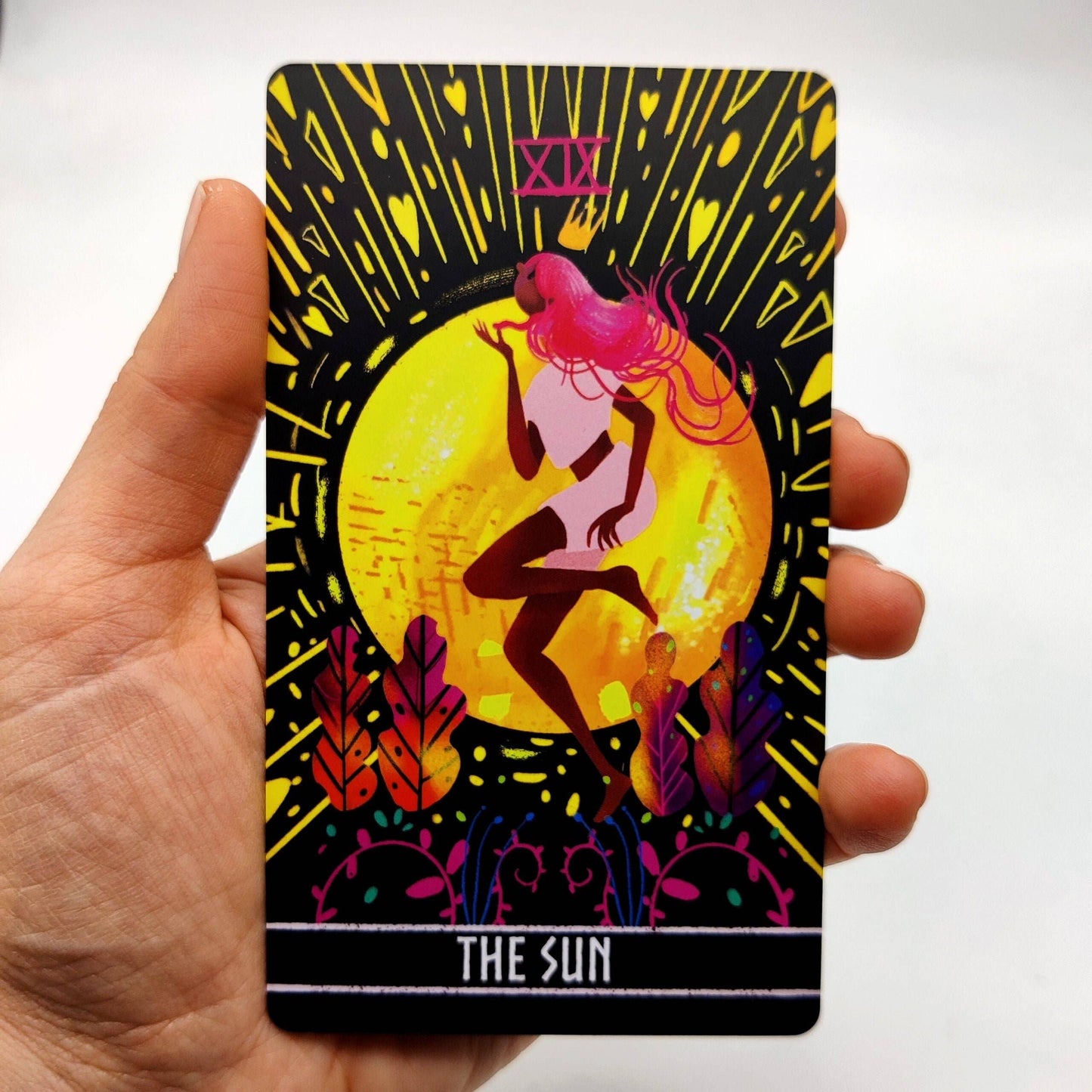 Tarot card titled 'The Sun' held by a hand on a white background