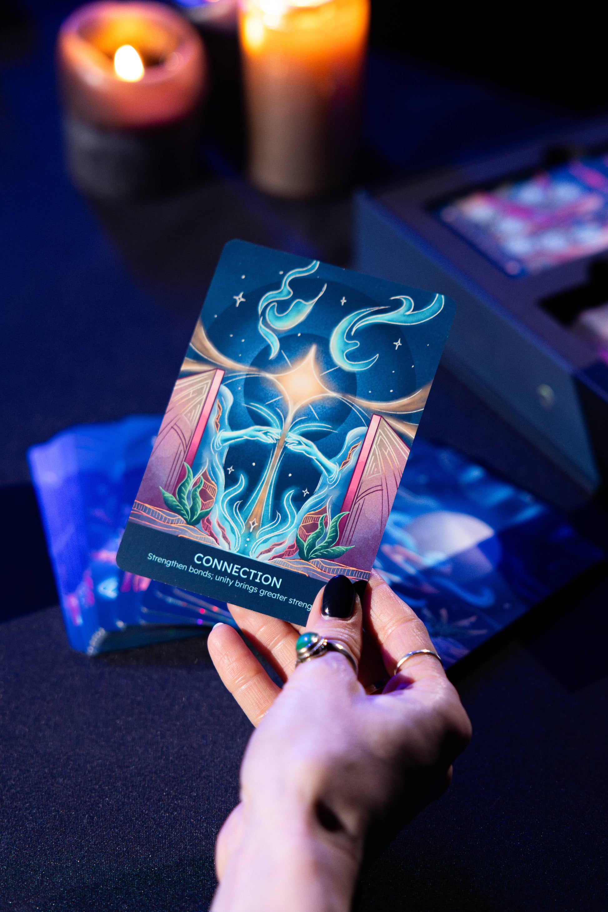 Hand holding a tarot card with candles and other cards in the background