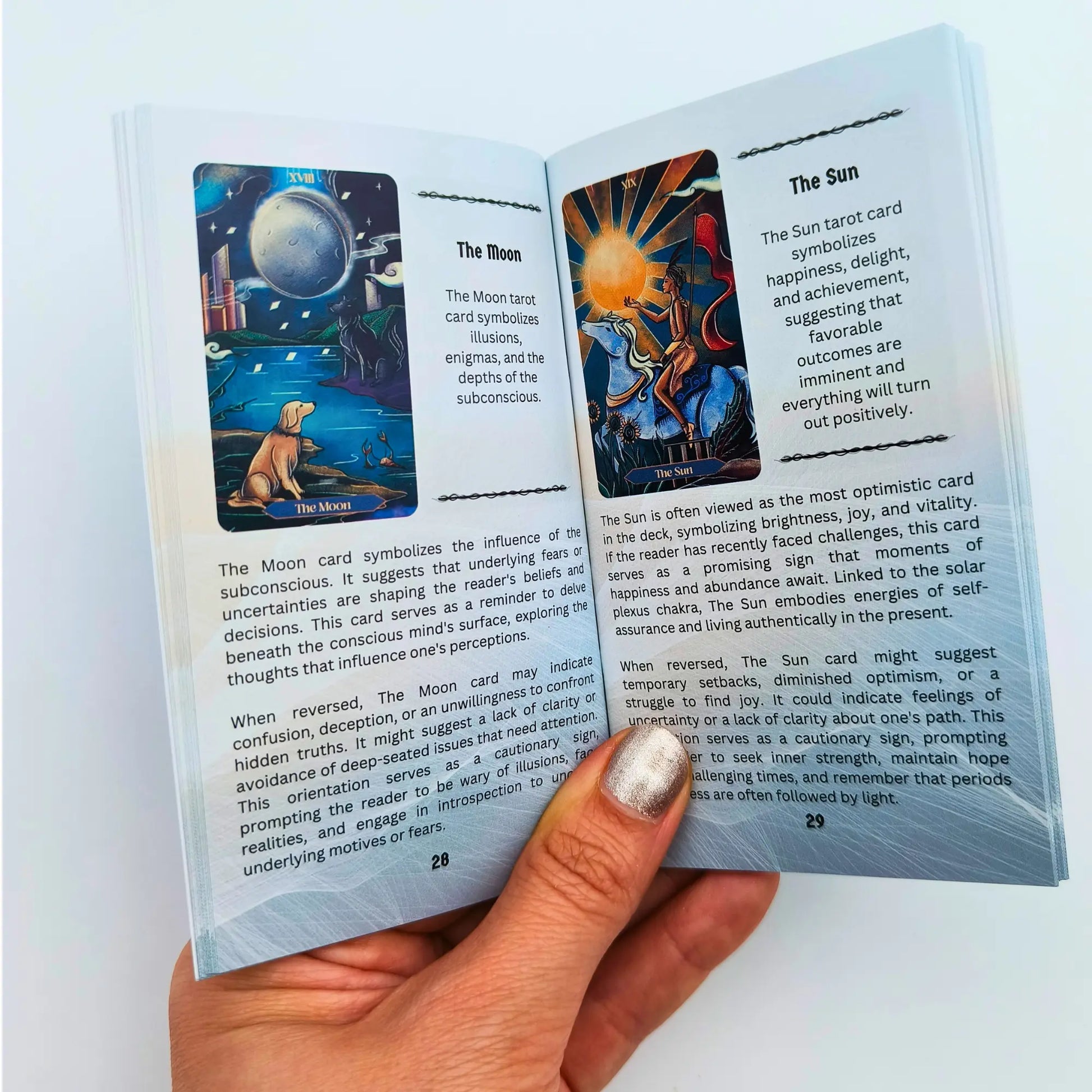 Open book with tarot cards and descriptions, held by a hand.