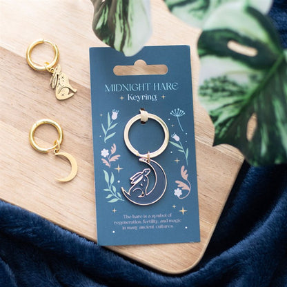 Gold keychain on a blue card with decorative elements, placed on a wooden surface with green leaves.