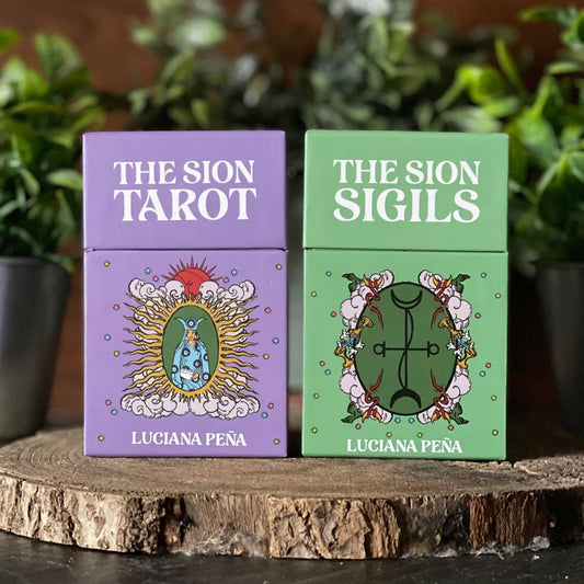 Two tarot card sets, 'The Sion Tarot' and 'The Sion Sigils', by Luciana Peá on a wooden surface with plants in the background.