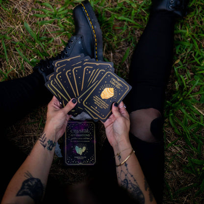 Person holding tarot cards on grass Gold Crystal Affirmations Golden Aura Edition featuring luxury affirmation cards inspired by crystal wisdom, mindfulness, and positive daily intentions.