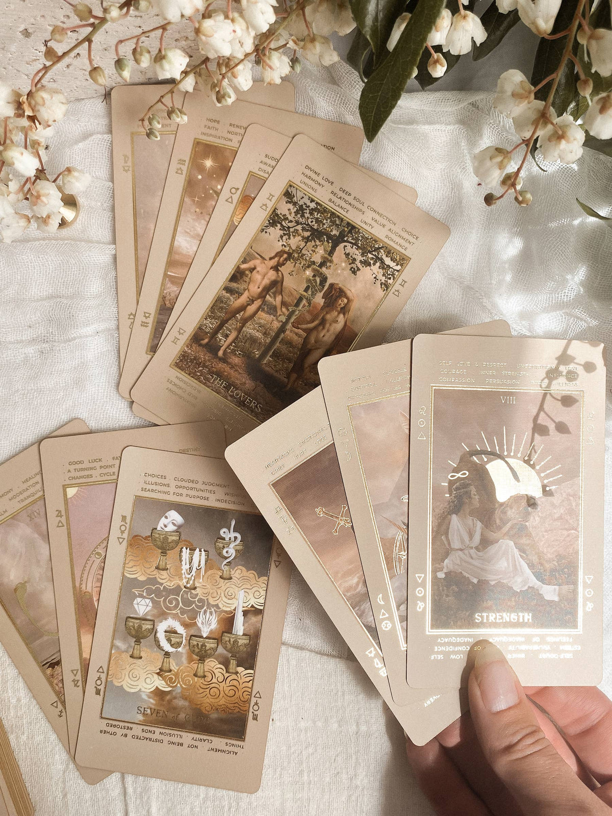 Collection of tarot cards on a textured surface with floral decorations Lucid Dreams Beginner's Tarot Beige Edition IV by ST. SOLEIL with gold foil cards, matte gold edges and guidebook