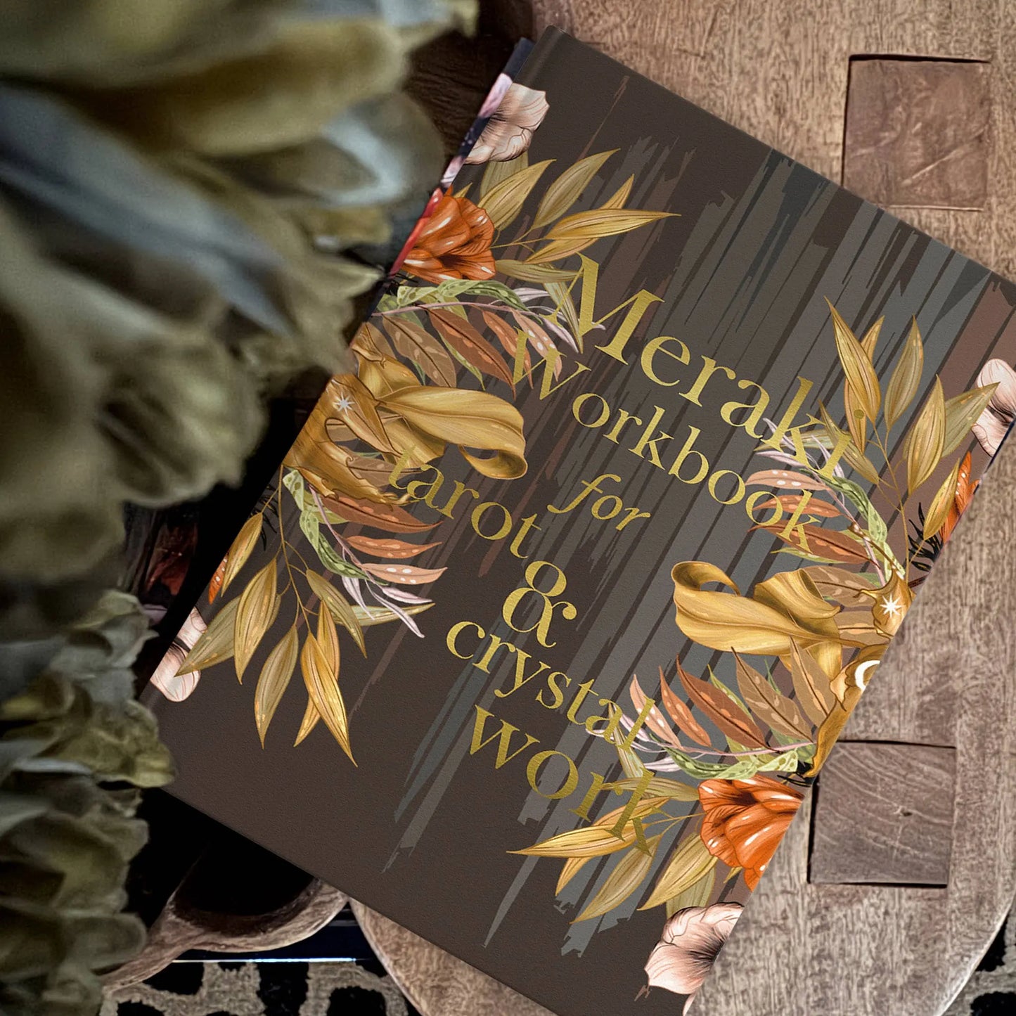 Book titled 'Meraki Workbook for Tarot & Crystal Wolf' with floral design on a wooden surface.