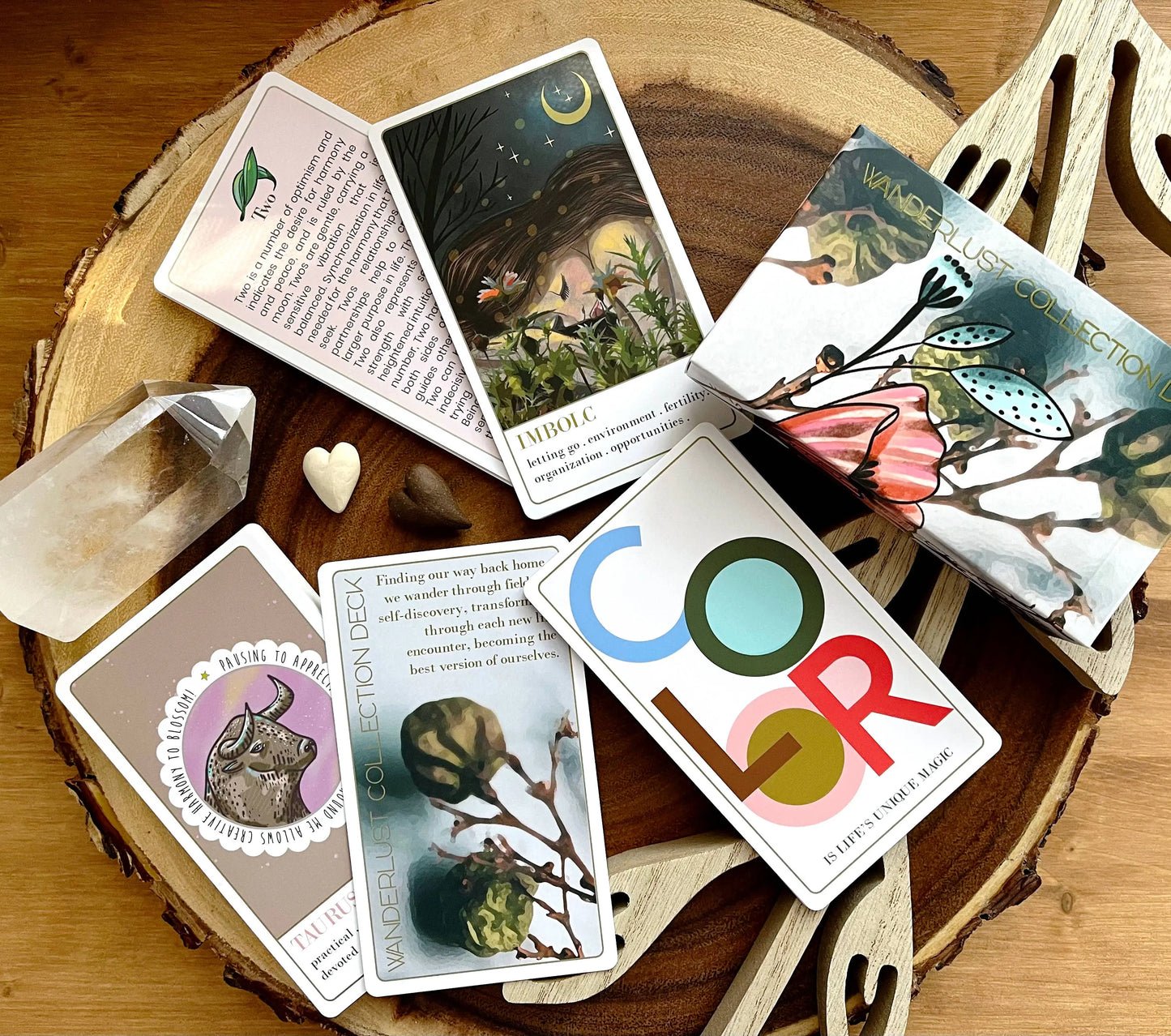 Collection of tarot cards on a wooden surface with a crystal and heart-shaped object. Wanderlust oracle deck