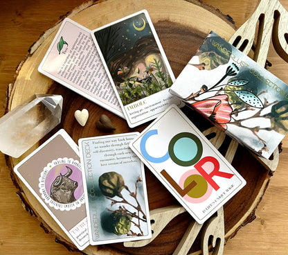 Collection of tarot cards on a wooden surface with a crystal and heart-shaped object. Wanderlust oracle deck