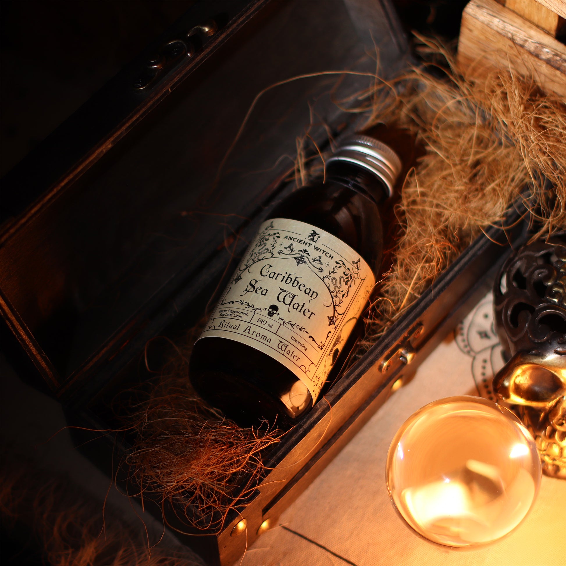 Bottle of 'Caribbean Sea Water' ritual water in a decorative box with hay, candlelight, and ornate elements.