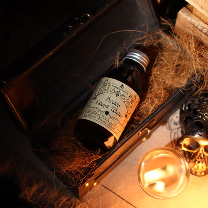 Bottle of Avalon Island Water with a label on a dark surface with hay and a candle.