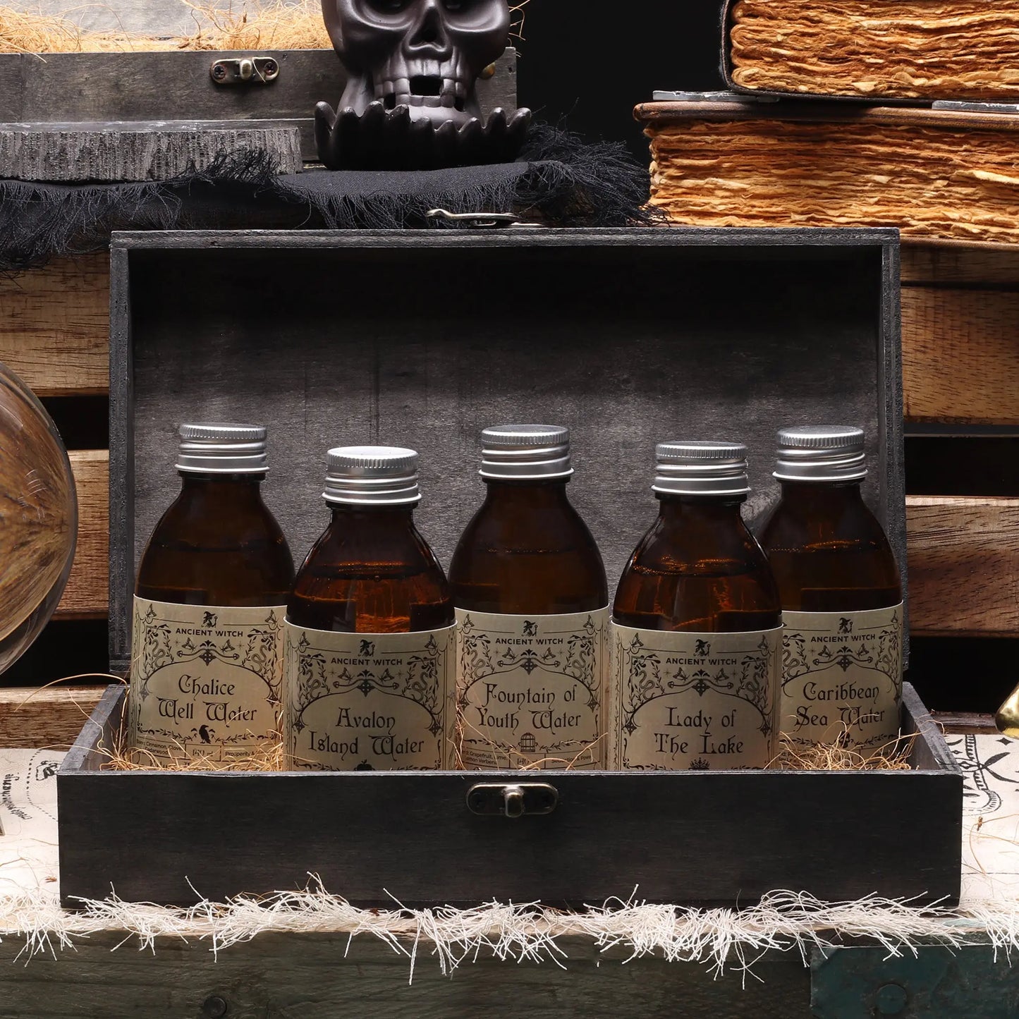 Five bottles with labels in a wooden box, surrounded by books and a skull.