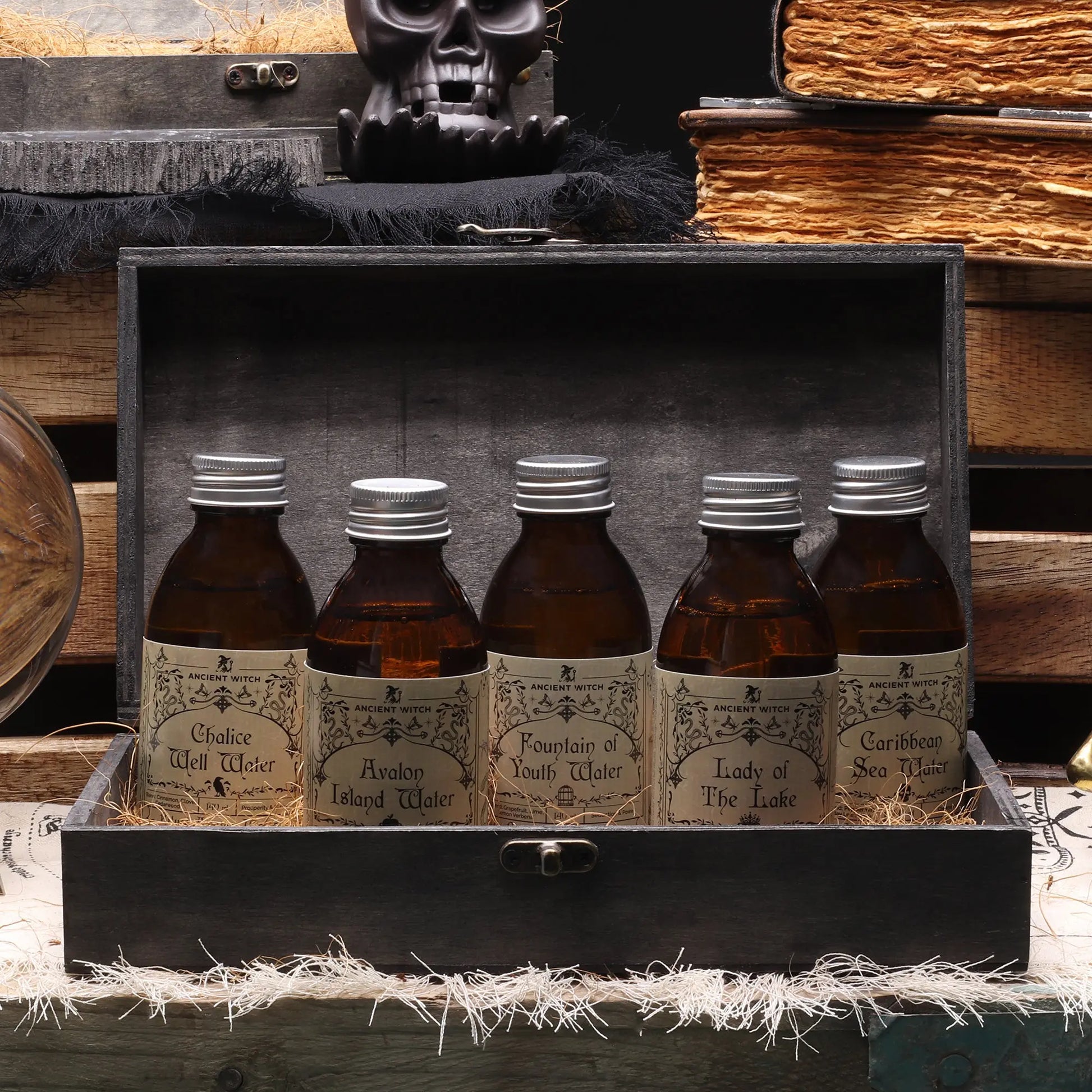 Five bottles with labels in a wooden box, surrounded by books and a skull.