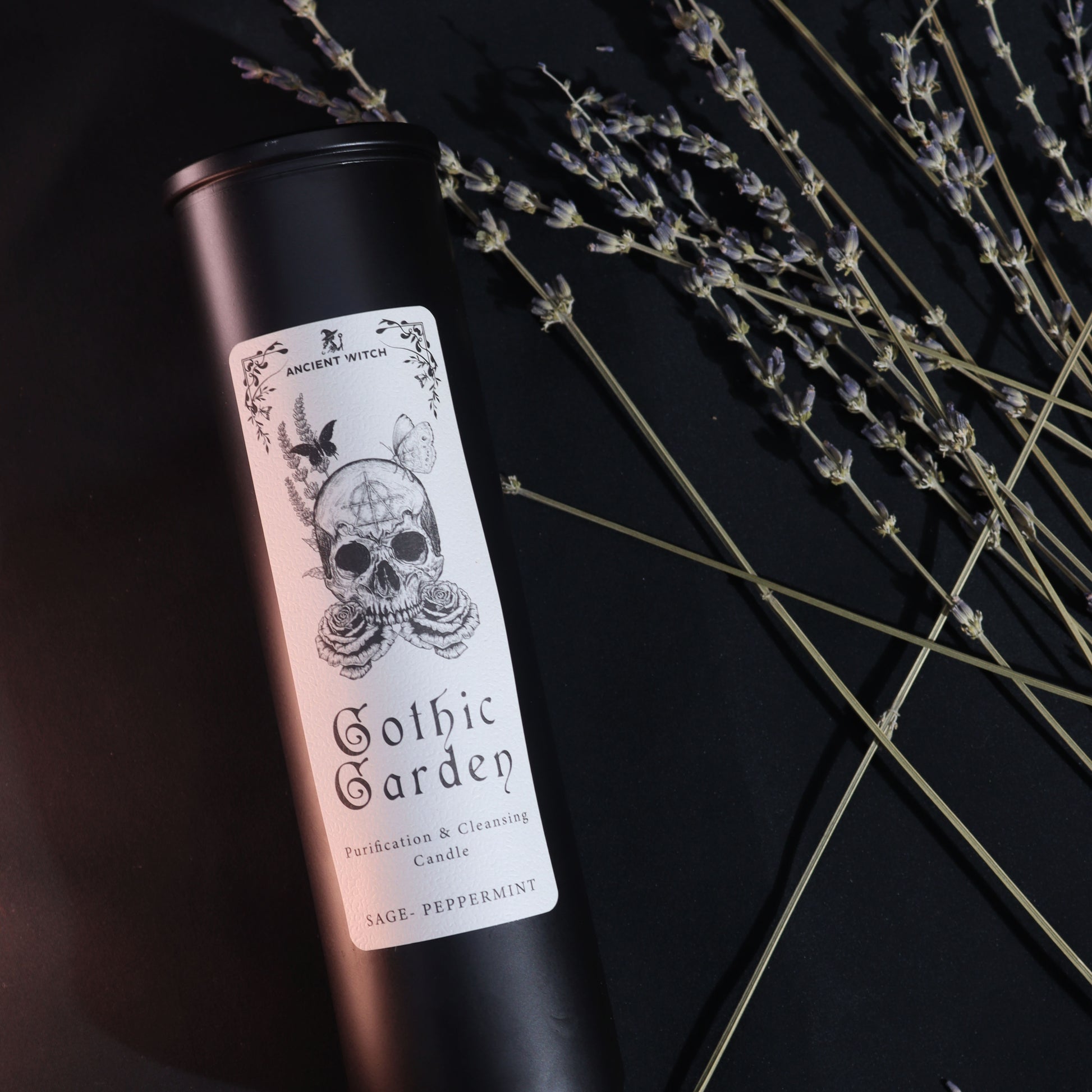 Candle in a black tin with a skull design on the label, set against a dark background with lavender.