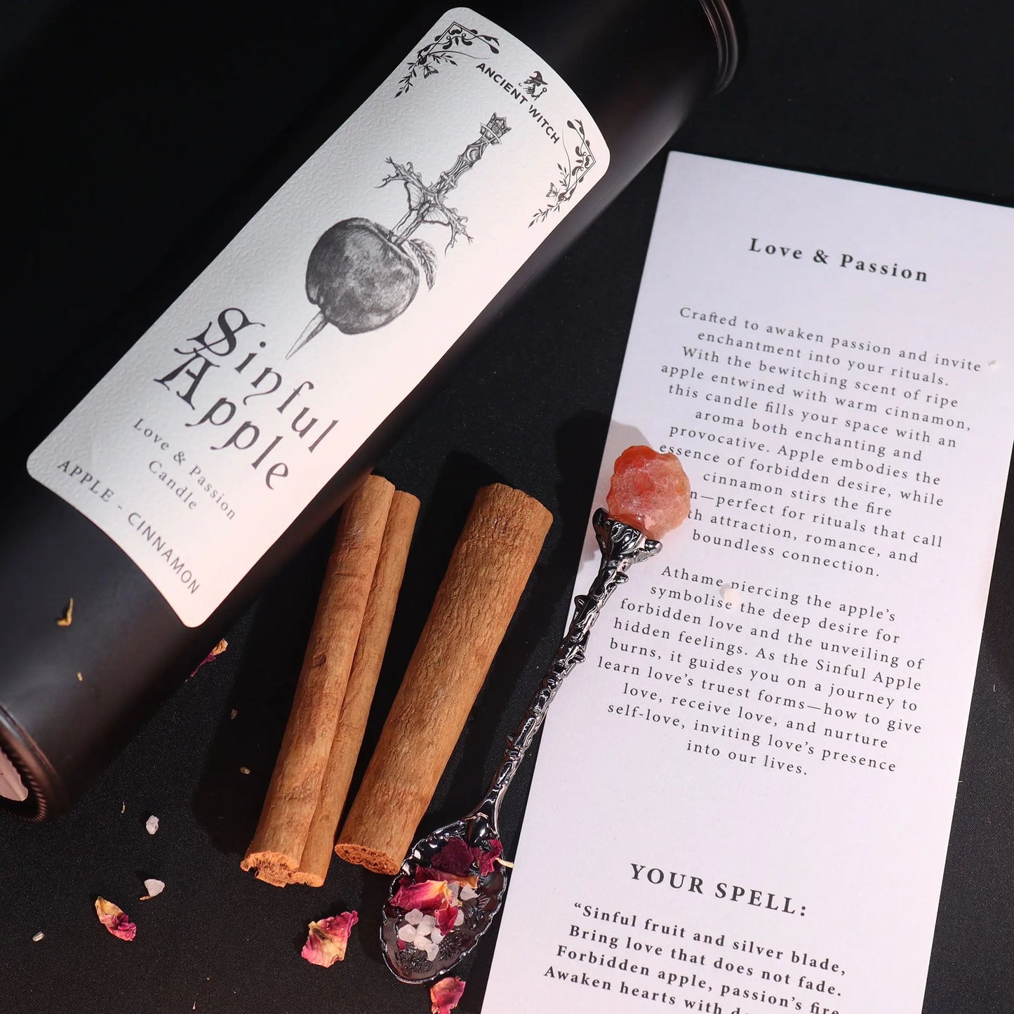 Candle labeled 'Sinful Apple' with cinnamon sticks and a spoon on a dark surface.