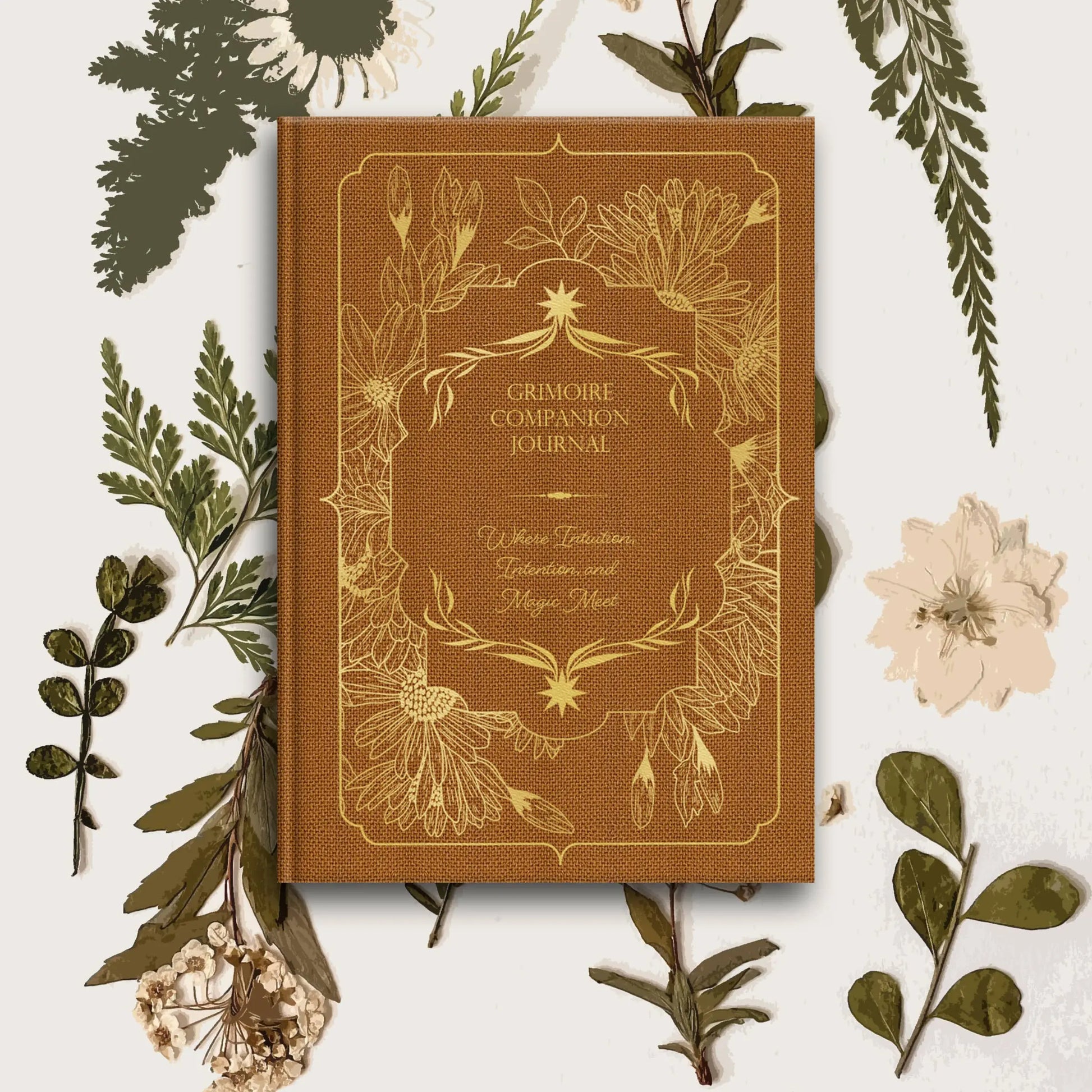 Brown 'Grimoire Companion Journal' surrounded by green leaves and flowers on a white background Grimoire Bouchette and Co Oneness Emporium