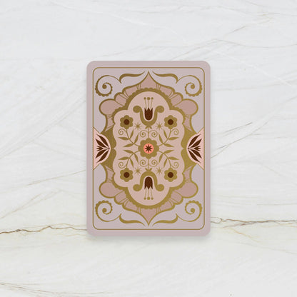 Decorative playing card with intricate gold and brown design on a white marble surface