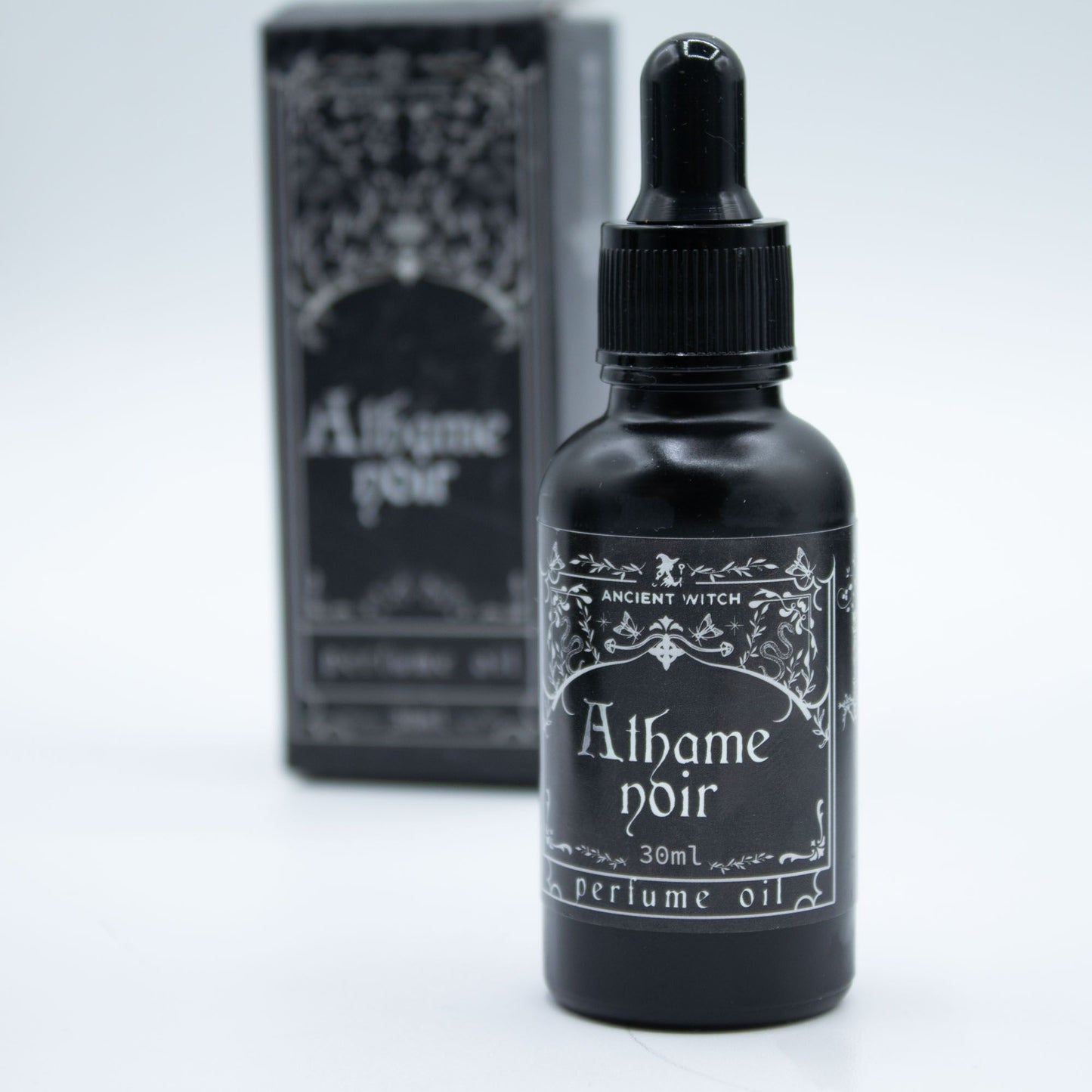 Black bottle of 'Athame Noir' perfume oil with a dropper and packaging on a light gray background