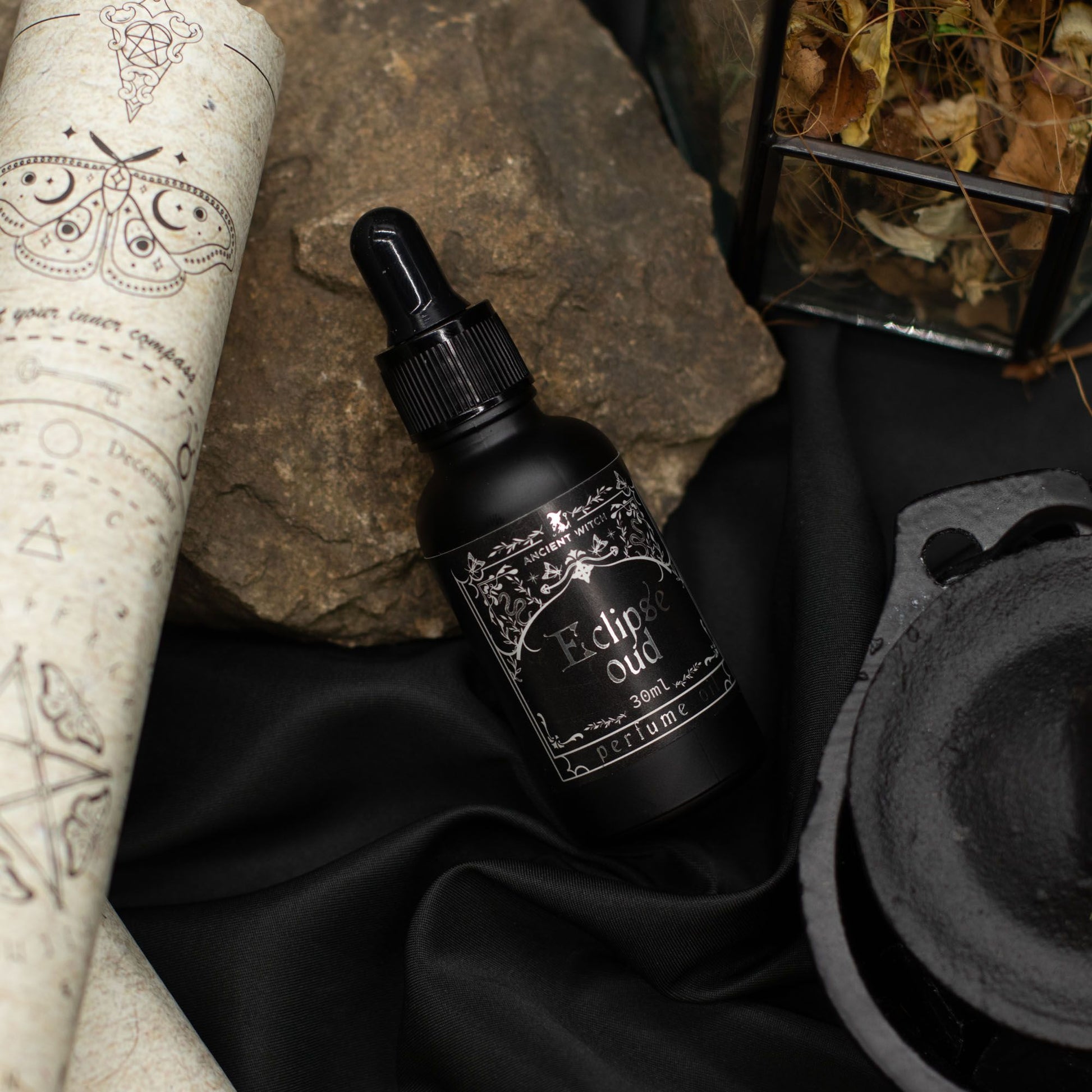 Black bottle labeled 'Eclipse Oud' on a dark fabric background with mystical elements.